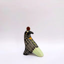 Ceramic sculpture of a black billed magpie, with stylized feather patterning in cream and mint green. On its back is a poppy flower and atop its head is a gold coin.