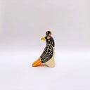 A stylized ceramic red-tailed hawk sculpture, with a black and beige body, yellow beak and tail accents, and a small gold coin on its head, photographed against a plain light gray background.