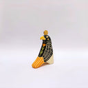 A stylized ceramic red-tailed hawk sculpture, with a black and beige body, yellow beak and tail accents, and a small gold coin on its head, photographed against a plain light gray background.