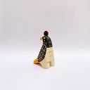 A stylized ceramic red-tailed hawk sculpture, with a black and beige body, yellow beak and tail accents, and a small gold coin on its head, photographed against a plain light gray background.