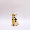 Cream colored ceramic sculpture of a bird, sitting in profile, with black and yellow feather detailings. It has a red cheek and a gold coin atop its head.