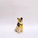 Cream colored ceramic sculpture of a bird, sitting in profile, with black and yellow feather detailings. It has a red cheek and a gold coin atop its head.