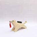 A ceramic sculpture shaped like a wolf, cream colored with gold color detailings. It carries a red tassel in its mouth and has a small wrapped doll-like object on its back.