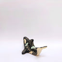 A ceramic orca sculpture with a black and cream body, decorated with cream sgraffito line art and flowers, and a turquoise tassel ornament on its side, set against a plain white background.