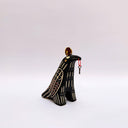 Ceramic sculpture of a black raven-like bird, with sgraffito line art, cream and red, on its feathers. It has a gold coin atop its head and a small key on a red string in its beak.