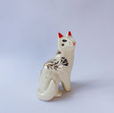 White ceramic figurine of a fox or cat with red ears and a gold leaf pattern on its body of poppy flowers and leaves.