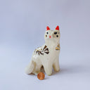 White ceramic figurine of a fox or cat with red ears and a gold leaf pattern on its body of poppy flowers and leaves.