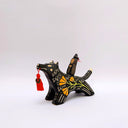 Ceramic sculpture of a wolf, black with cream colored sgraffito fur textures. It has a poppy flower design on its side and on its back is a doll charm of a woman, with a tiny wolf's mask atop her head. The wolf has a red tassel in its mouth.