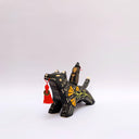 Ceramic sculpture of a wolf, black with cream colored sgraffito fur textures. It has a poppy flower design on its side and on its back is a doll charm of a woman, with a tiny wolf's mask atop her head. The wolf has a red tassel in its mouth.