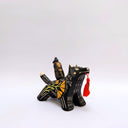 Ceramic sculpture of a wolf, black with cream colored sgraffito fur textures. It has a poppy flower design on its side and on its back is a doll charm of a woman, with a tiny wolf's mask atop her head. The wolf has a red tassel in its mouth.