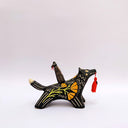 Ceramic sculpture of a wolf, black with cream colored sgraffito fur textures. It has a poppy flower design on its side and on its back is a doll charm of a woman, with a tiny wolf's mask atop her head. The wolf has a red tassel in its mouth.