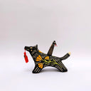 Ceramic sculpture of a wolf, black with cream colored sgraffito fur textures. It has a poppy flower design on its side and on its back is a doll charm of a woman, with a tiny wolf's mask atop her head. The wolf has a red tassel in its mouth.