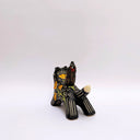 Ceramic sculpture of a wolf, black with cream colored sgraffito fur textures. It has a poppy flower design on its side and on its back is a doll charm of a woman, with a tiny wolf's mask atop her head. The wolf has a red tassel in its mouth.