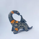 Ceramic sculpture of a black dinosaur with a long neck, looking to its own back which has a baby dinosaur standing on it. Both dinosaurs have a carved patterning of orange poppies with cream colored stylistic lines.