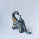 Ceramic sculpture of a black dinosaur with a long neck, looking to its own back which has a baby dinosaur standing on it. Both dinosaurs have a carved patterning of orange poppies with cream colored stylistic lines.