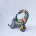 Ceramic sculpture of a black dinosaur with a long neck, looking to its own back which has a baby dinosaur standing on it. Both dinosaurs have a carved patterning of orange poppies with cream colored stylistic lines.