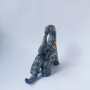 Ceramic sculpture of a black dinosaur with a long neck, looking to its own back which has a baby dinosaur standing on it. Both dinosaurs have a carved patterning of orange poppies with cream colored stylistic lines.
