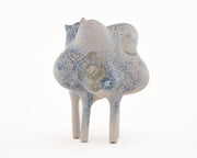 Ceramic sculpture of a character with a lumpy spotted body, tall thin legs, and small eyes and ears.