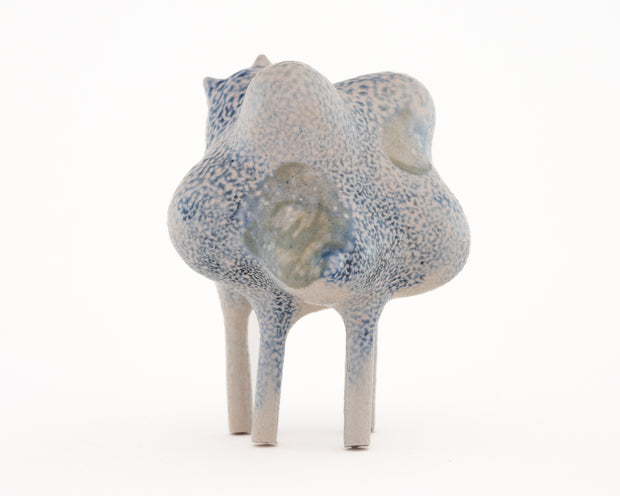 Ceramic sculpture of a character with a lumpy spotted body, tall thin legs, and small eyes and ears.