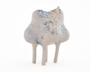 Ceramic sculpture of a character with a lumpy spotted body, tall thin legs, and small eyes and ears.