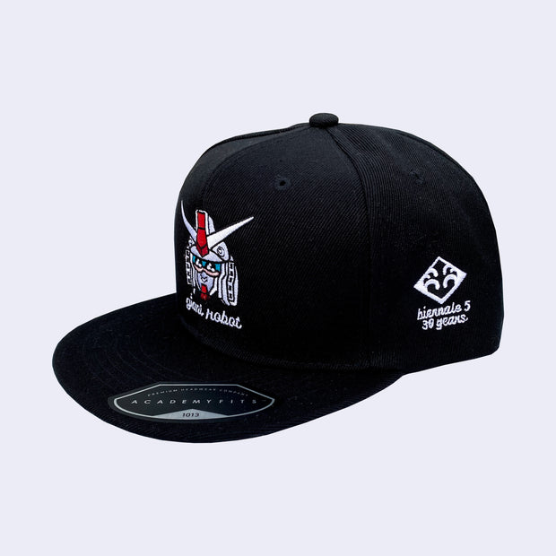 Black cap with an embroidery of a white gundam head with cute kawaii eyes and a smile. Below is "giant robot" written in white lower case cursive. Side of cap has JANM logo and "biennale 5 30 years" written in lowercase white cursive.