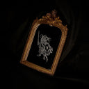 An ornate gold-framed mirror featuring a white line-art engraving of a mouse warrior on a black background, set against a dark draped fabric backdrop.