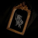 An ornate gold-framed mirror featuring a white line-art engraving of a mouse warrior on a black background, set against a dark draped fabric backdrop.