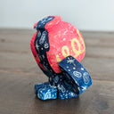 Whittled sculpture of a character with a  red vessel pouring out patterned water as its head and its body made out of the same water patterning. It's head has a sad expression and gold colored accents and it sits and holds its head in its hands. 