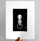 Ink drawing on white paper of a human like character with a round, planet like head and large semi circle eyes. It sits with its knees pulled into its chest on a small planet.