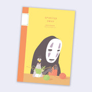 Yellow notebook with orange binding featuring an illustration of No Face from Spirited Away, sitting at a table knitting with a small mouse and bird.
