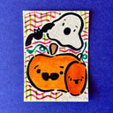 Artwork featuring a cute Halloween illustration with a white ghost, black bat, orange pumpkin, and smaller orange fruit on a patterned background, displayed on a textured blue surface.