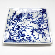 White porcelain plate with stark blue line illustration of 3 girls with robotic helmets, seen only from the neck up. A fish is positioned across the plate with a bird below it. Shown at an angle.