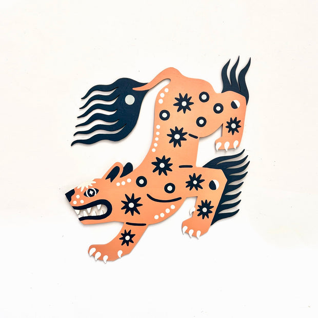 Die cut, brightly painted wooden sculpture of a folklore style panther, orange with navy blue and white patterning. It has star burst and moon patterns on its body, with wild navy blue tail and mane and body hair. 