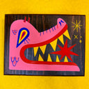 Artwork on a wooden panel of a pink monster creature's head, turned to the side and eating a large red star.
