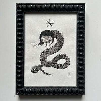 Framed artwork of a stylized illustration with a snake with 2 pairs of eyes and long black hair.