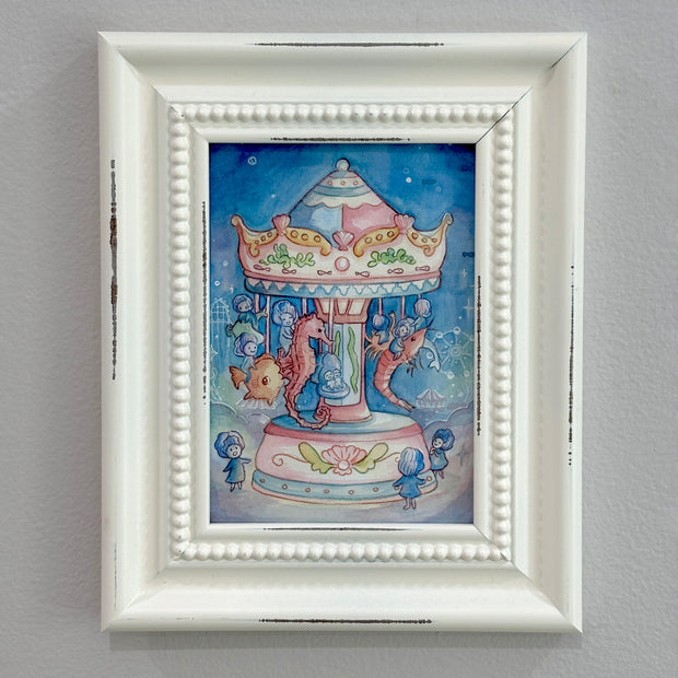 Framed artwork of a colorful carousel with seahorses and little shell children riding them on a gray wall.