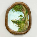 An oval wooden frame containing a whimsical painted scene of a character fishing from a tree branch, displayed on a white wall.
