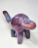 Purple and blue glossy ceramic sculpture of a long neck dinosaur with a simplistic, cute face.