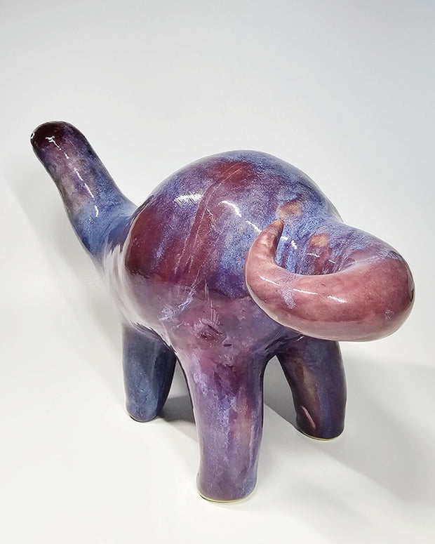Purple and blue glossy ceramic sculpture of a long neck dinosaur with a simplistic, cute face.