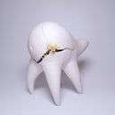 White ceramic sculpture of a quadruped creature with a large humped body, curved tall legs and a long neck. It has cracks running through its body and inside of it grows flowers. 