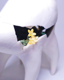 White ceramic sculpture of a quadruped creature with a large humped body, curved tall legs and a long neck. It has cracks running through its body and inside of it grows flowers. 