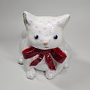 White cat-shaped ceramic sculpture with pink glitter specks, wearing a sparkly red bow.