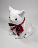 White cat-shaped ceramic sculpture with pink glitter specks, wearing a sparkly red bow.