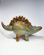 Glossy, multicolor ceramic sculpture of a dinosaur with many spikes on its long back like a stegosaurus. 