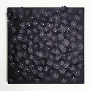 Black wooden panel covered in small glittery black flowers cut out of paper and adhered, coating most of the panel's surface. Each flower has a small gem as the center.