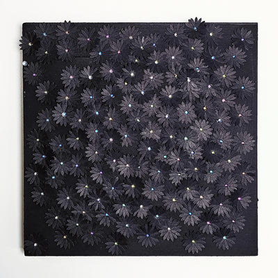 Black wooden panel covered in small glittery black flowers cut out of paper and adhered, coating most of the panel's surface. Each flower has a small gem as the center.