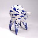 Ceramic sculpture of a white quadruped creature with blue glossy designs on its body of fish and coral, the fish swimming amongst bubbles.