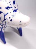 Ceramic sculpture of a white quadruped creature with blue glossy designs on its body of fish and coral, the fish swimming amongst bubbles.