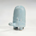 Ceramic turtle figurine with a light blue glaze and a subtle design of hills and houses on a white background