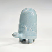 Ceramic turtle figurine with a light blue glaze and a subtle design of hills and houses on a white background